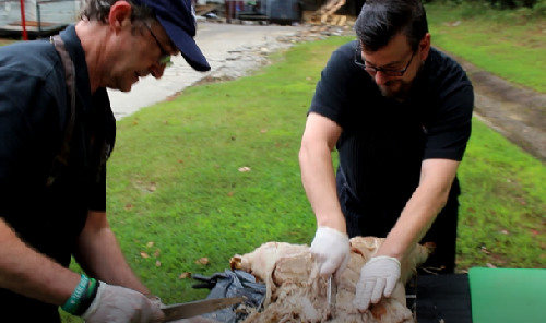 Former chef Bernard “Bernie” McDonough (right) took a break from sales calls to help Bill Brown chop up a magnificently roasted pig.

