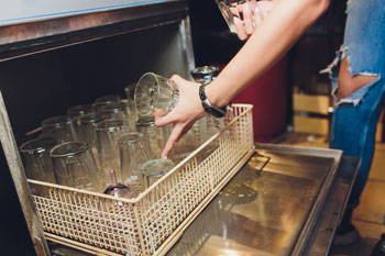 Restauarant employee quickly reloads an undercounter warewasher at the bar.
